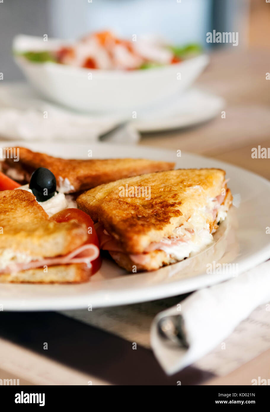 Eine Platte mit einem köstlichen Schinken Panini mit Tomate, Mozzarella, Oliven und Mayonnaise, serviert mit einem Beilagensalat Stockfoto