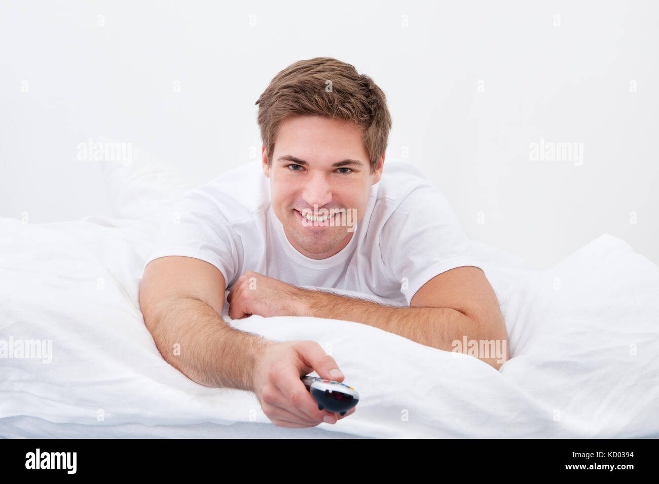 Junger Mann auf Bett Kanal mit Fernbedienung Stockfoto