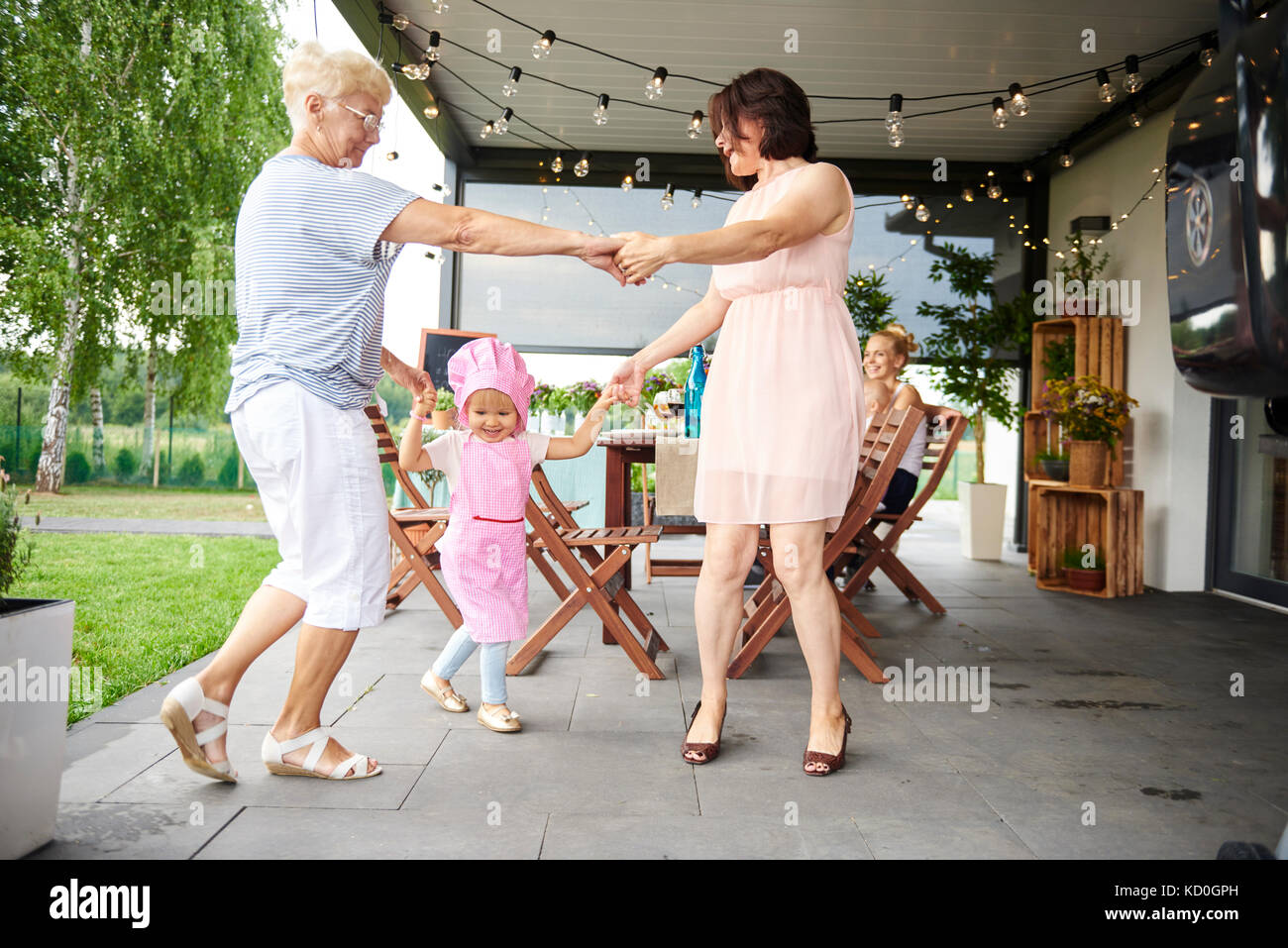 Senior und reife Frauen tanzen mit weiblichen Kleinkind bei Familie Mittagessen auf der Terrasse Stockfoto