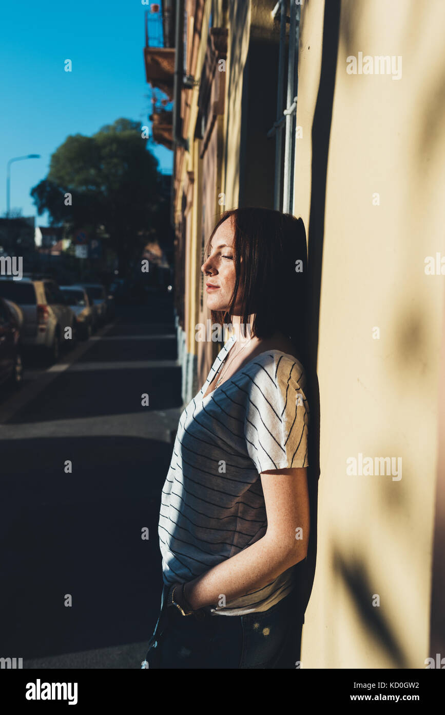 Junge Frau gegen sonnenbeschienenen Wand lehnt Stockfoto
