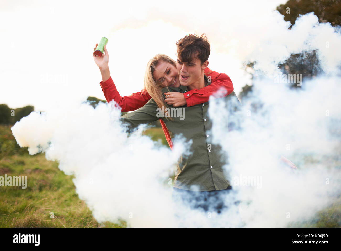 Junges Paar mit Austritt von Rauch aus Rauch flares im Feld umgeben Stockfoto