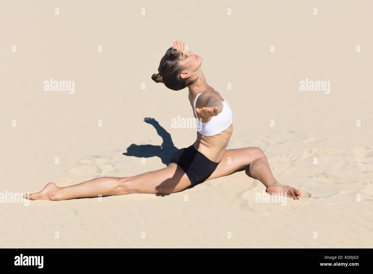Seitenansicht der Frau am Strand tun die Splits, die Arme öffnen sich in Yoga Position Stockfoto