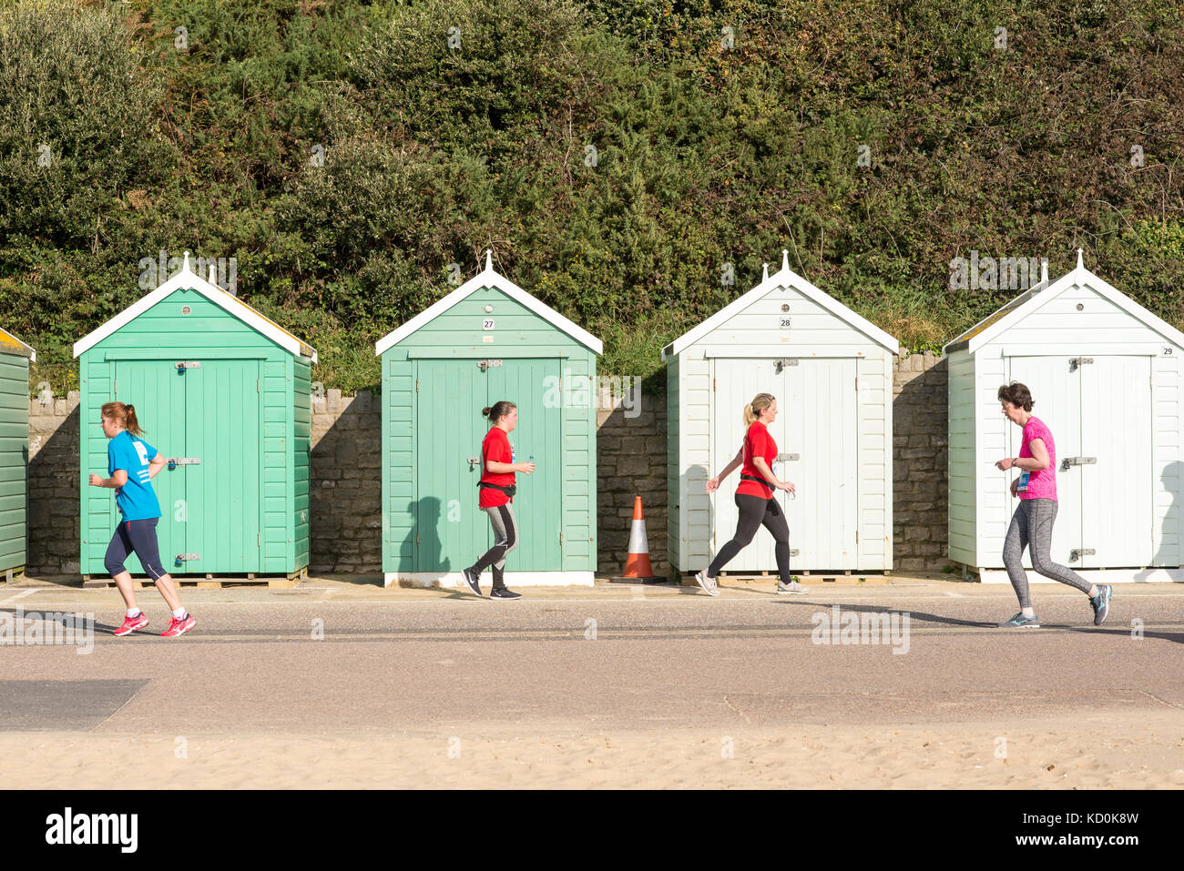 Bournemouth, Dorset, Großbritannien, 8.. Oktober 2017. Läufer, die am Bournemouth Marathon Festival teilnehmen, passieren Strandhütten auf der Promenade. In entgegengesetzte Richtungen laufen. Symmetrisch. Stockfoto