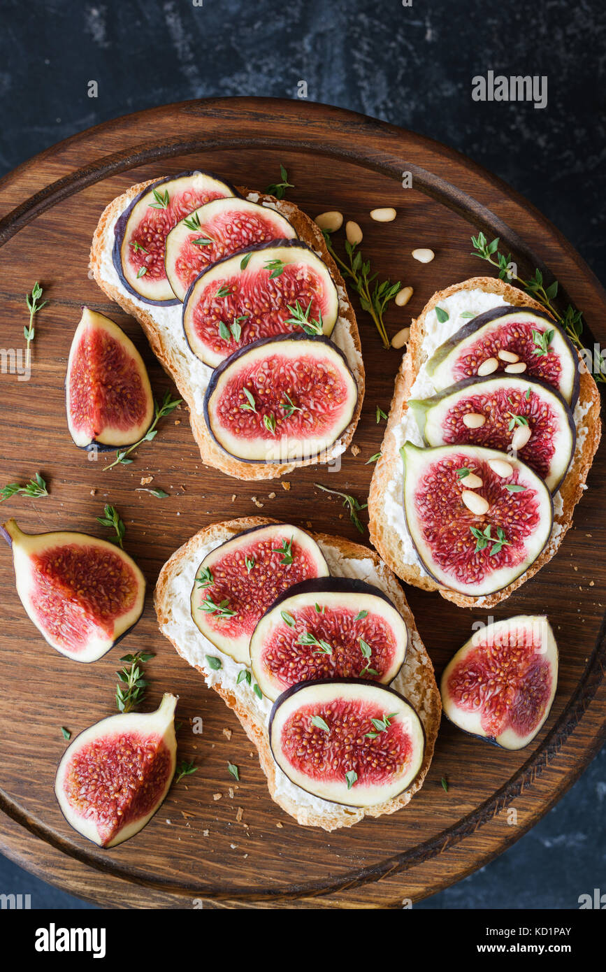 Bruschetta mit frischem lila Feigen, ricotta Käse und Honig auf Holz Schneidebrett garniert mit frischem Thymian und Pinienkernen. gesund Gourmet Snack oder Stockfoto