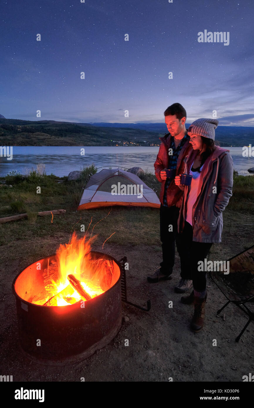Paar in der Nähe von Lagerfeuer. In der Abenddämmerung, trinken heiße Getränke Stockfoto