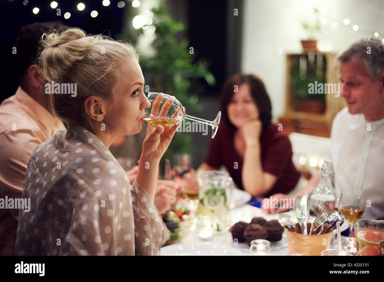 Gruppe von Menschen, die am Tisch sitzen, genießen Essen, junge Frau trinkt aus Glas Wein Stockfoto