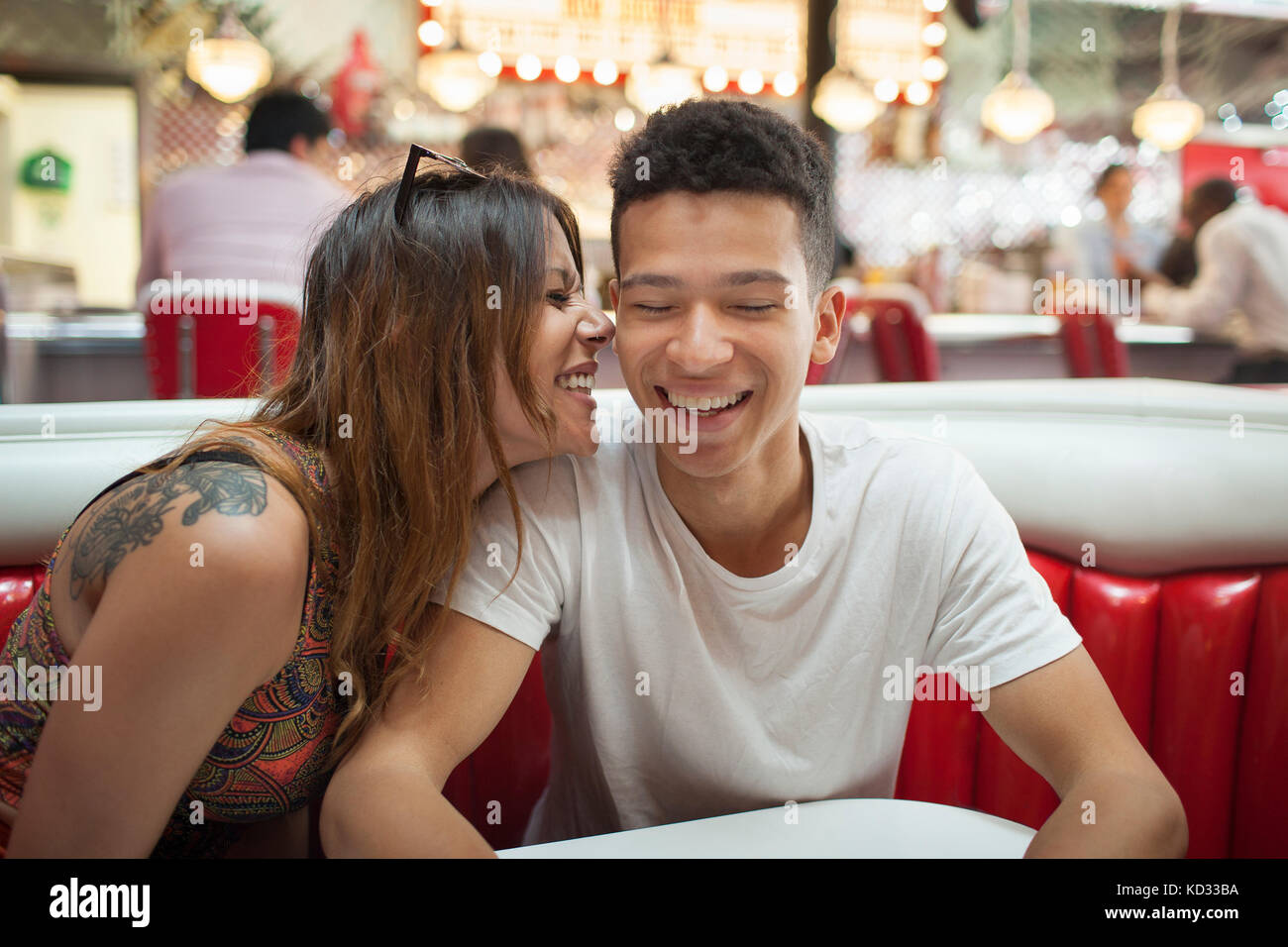 Junges Paar in Diner sitzen, junge Frau das Flüstern im Ohr des Menschen, Lachen Stockfoto