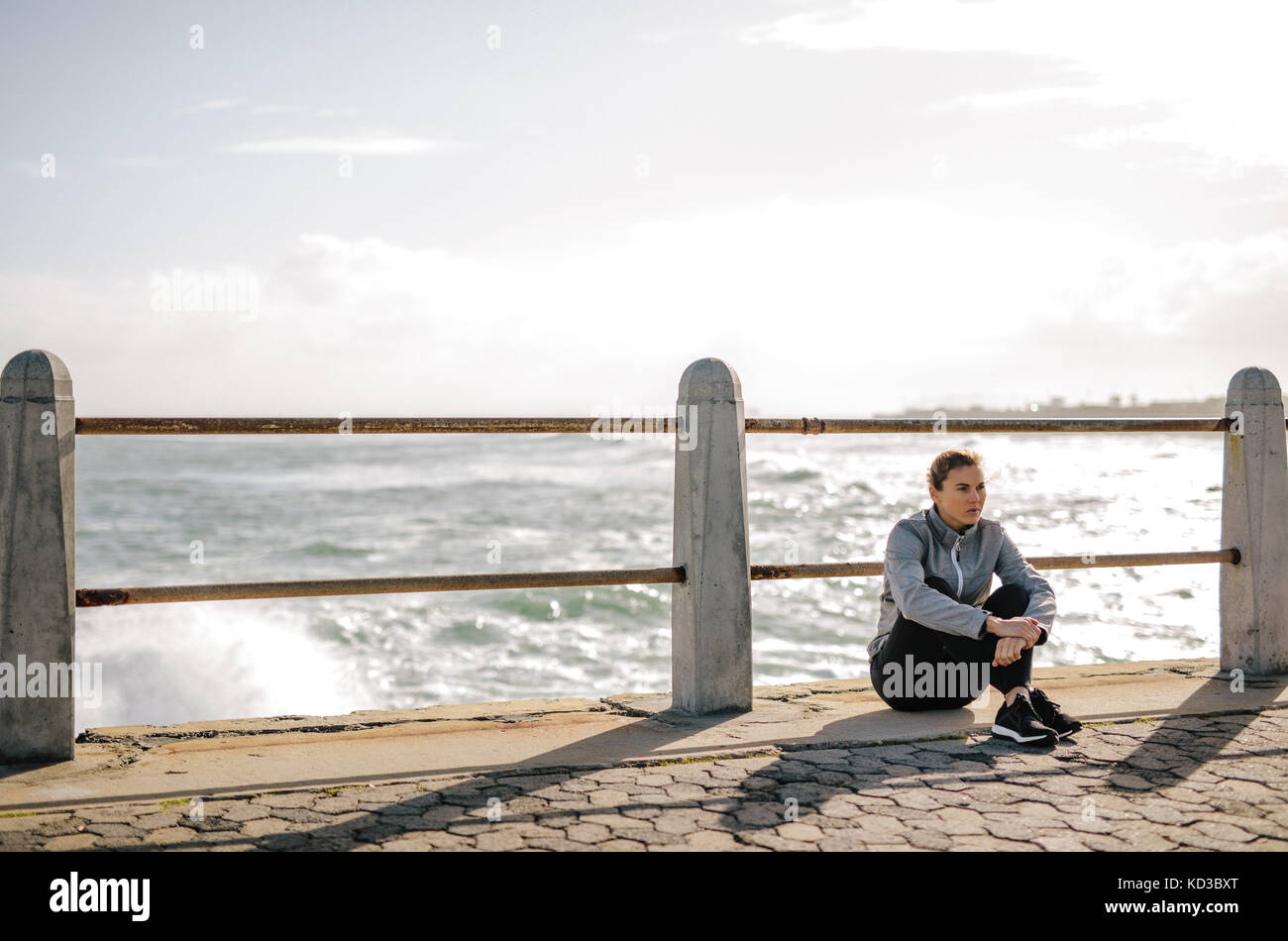 Frau Entspannung nach dem Training auf der Straße durch das Meer. Sportlerin, die Pause nach dem Fitness Training im Freien durch das Meer. Stockfoto