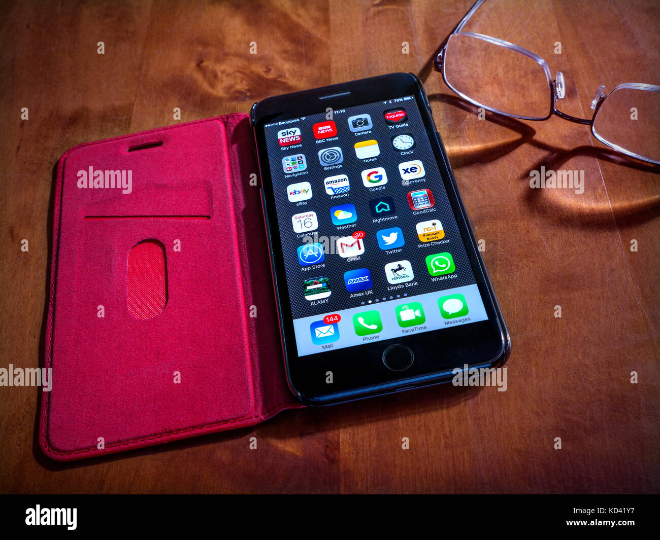 Smartphone-Apps iPhone 7 Plus Schwarz mit Bildschirmapplikationen, in roter Lederhülle auf dem Tisch, mit Lesebrille an der Seite. Stockfoto