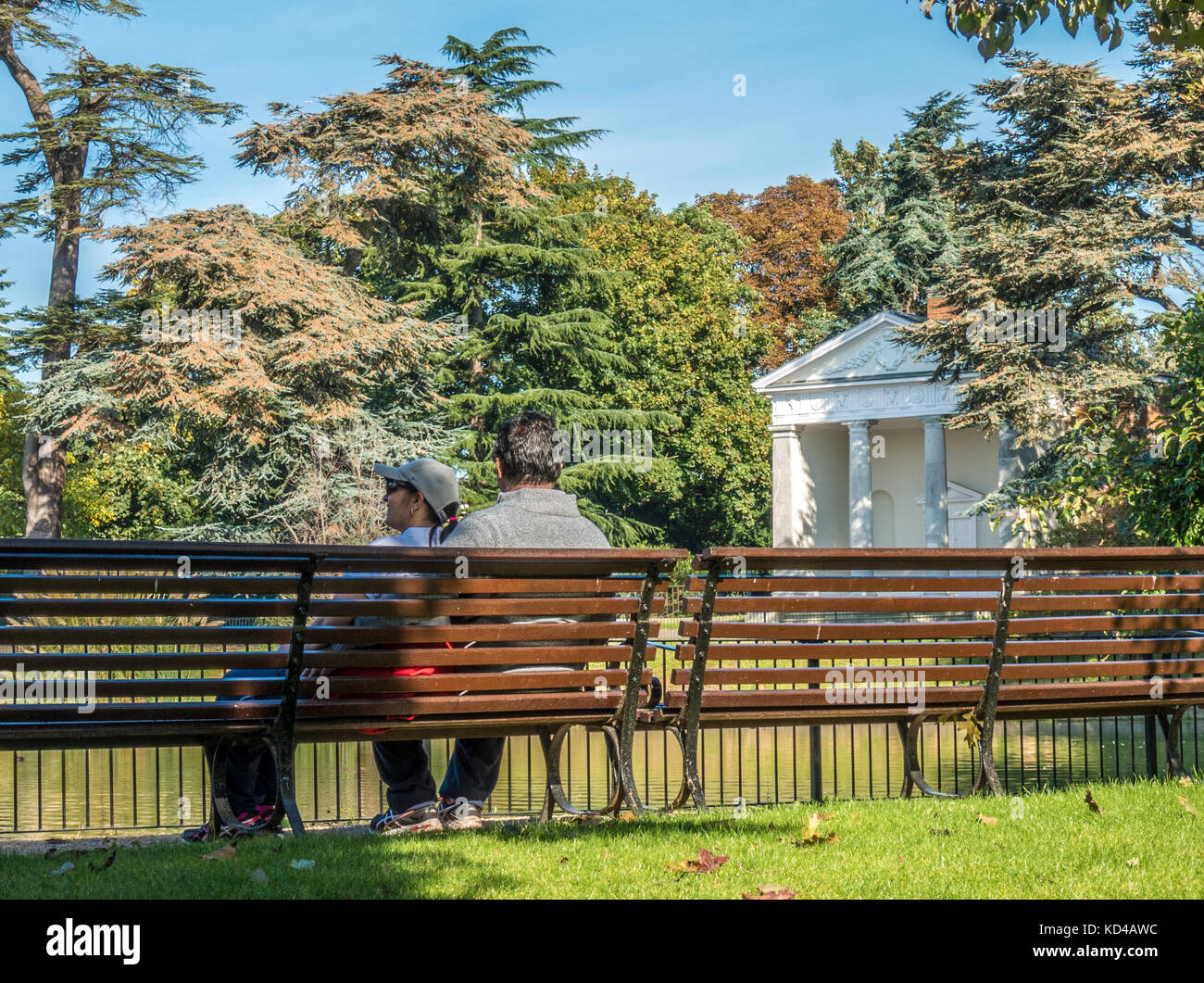 Asiatische Paar auf einer Bank sitzen in der warmen Frühherbst morgen Sonnenschein, neben der historischen Tempel in Gunnersbury Park, West London, England, UK. Stockfoto