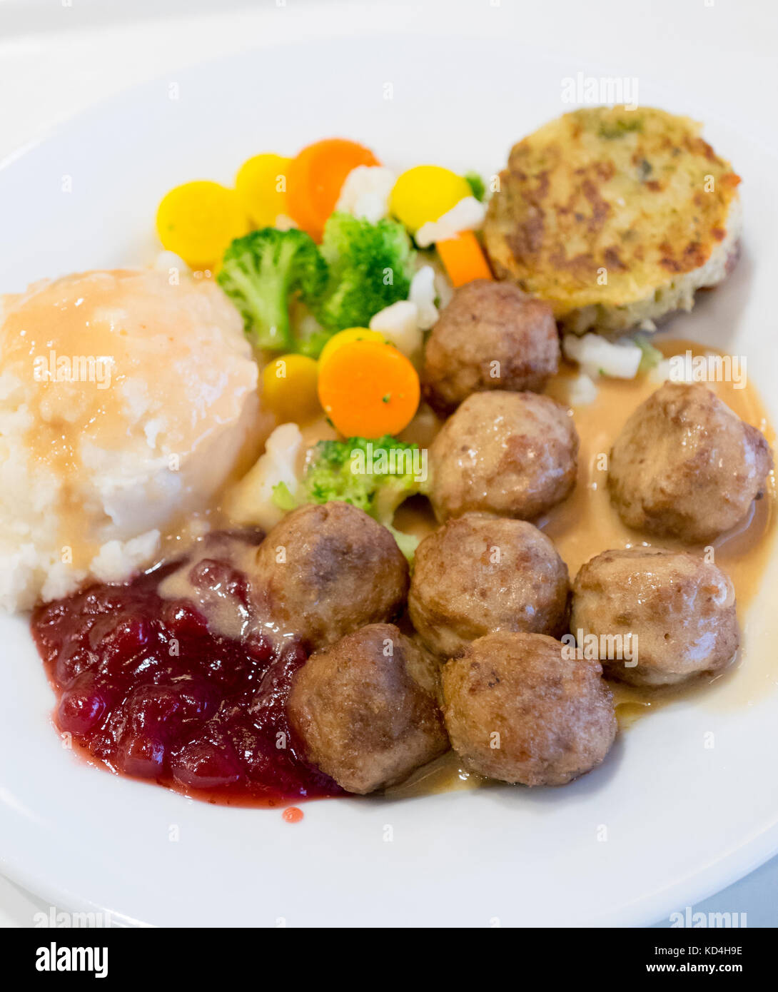 Ein Teller mit IKEA Fleischbällchen, Kartoffelpüree, Sahnesauce, Preiselbeersauce, gemischtem Gemüse und einem Kartoffel-Gemüse-Medaillon (grönsakskaka). Stockfoto