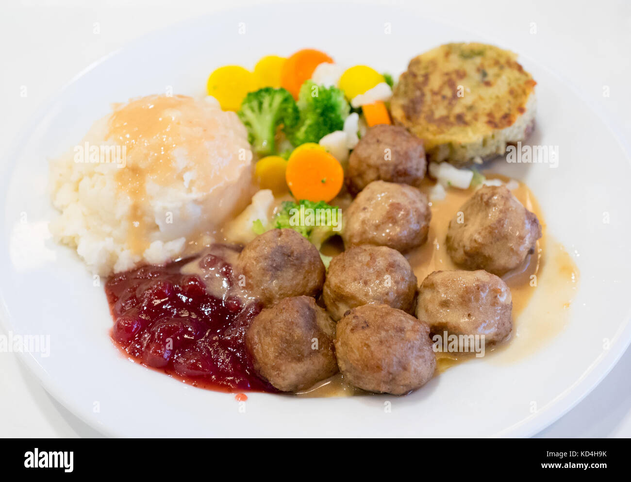 Ein Teller mit IKEA Fleischbällchen, Kartoffelpüree, Sahnesauce, Preiselbeersauce, gemischtem Gemüse und einem Kartoffel-Gemüse-Medaillon (grönsakskaka). Stockfoto