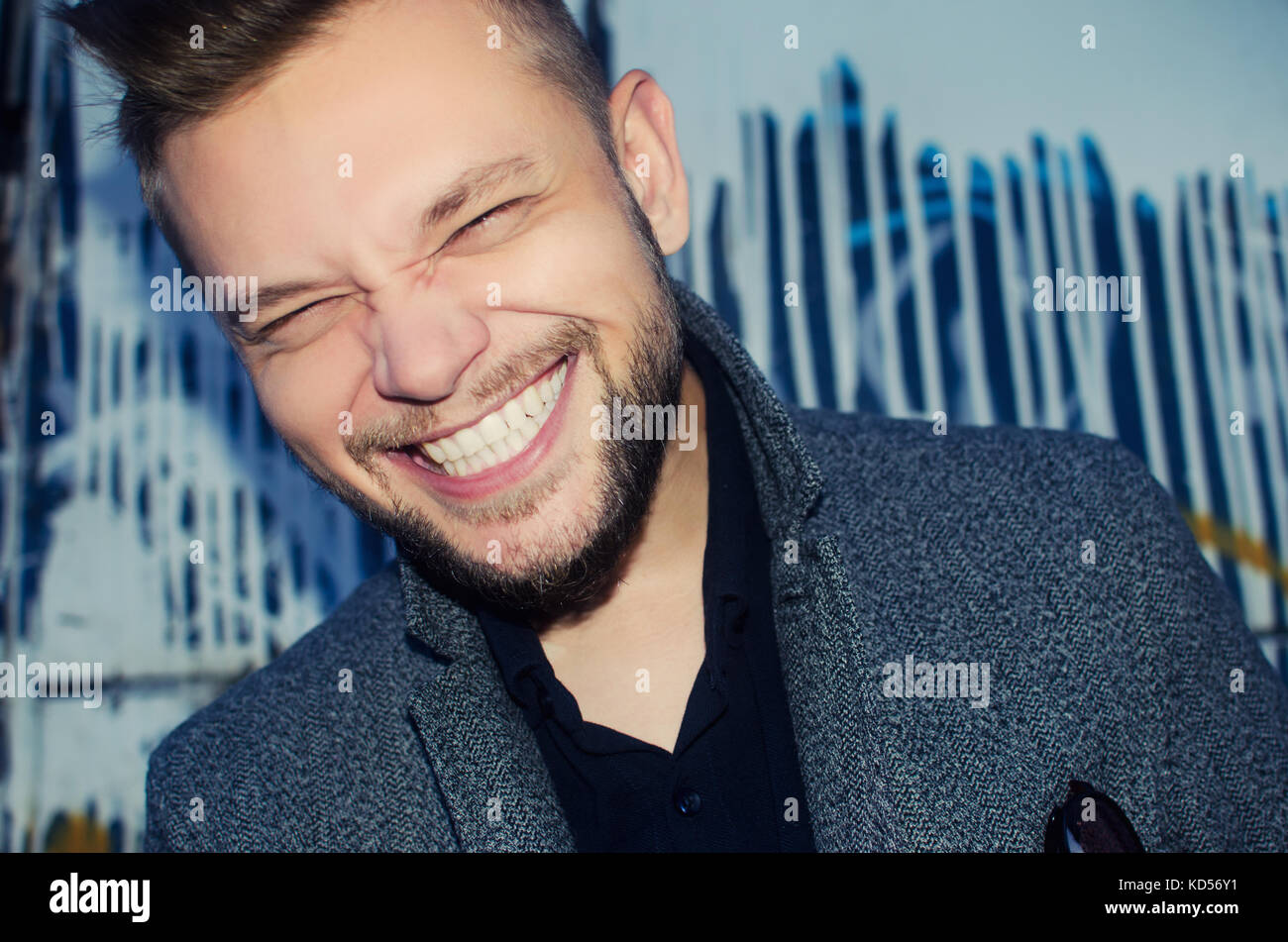 Positive Laughing Man mit einem weißen Zähnen Lächeln auf dem Hintergrund einer bemalten Wand Stockfoto