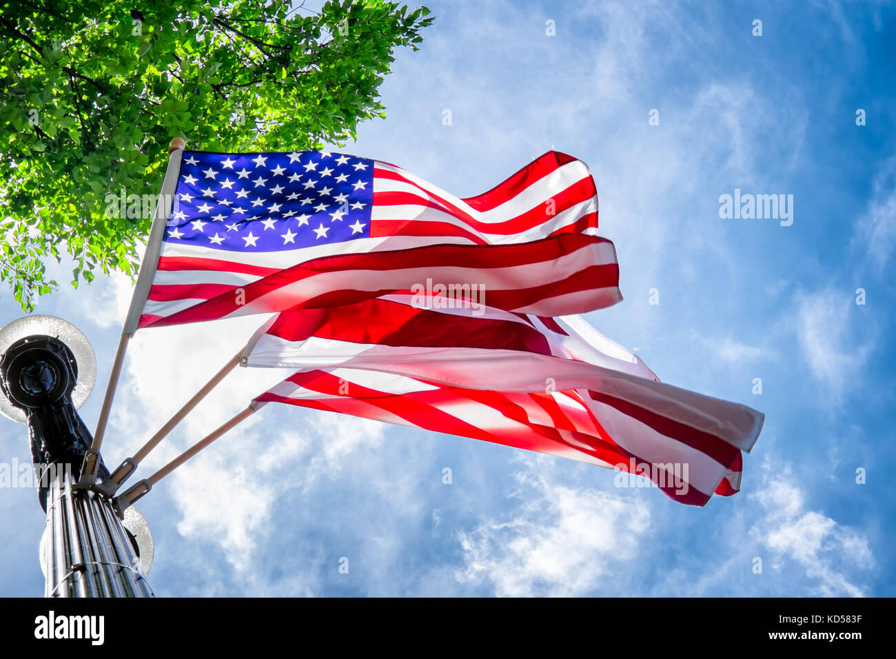 Amerikanische Fahnen winkend aus einem lichtmast in Washington DC. Ansicht von unten nach oben. Breezy Tag mit wispy Wolken und blauer Himmel. Straße Dekorationen Stockfoto