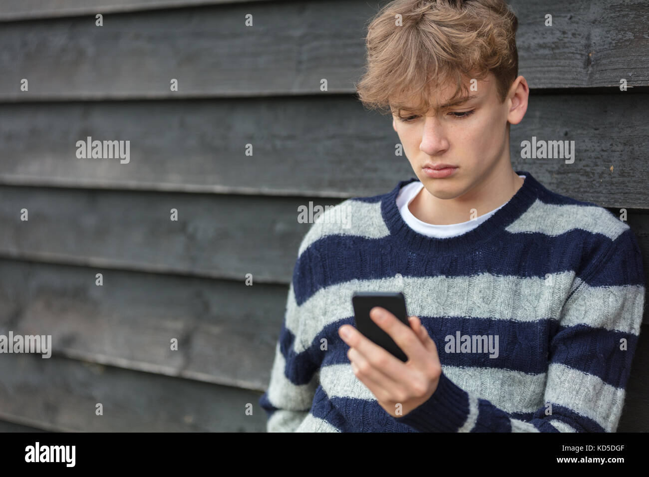 Traurig, deprimiert nachdenklich männliche junge Teenager blonde Kind außerhalb mit Handy für SMS-Nachrichten oder Social Media Stockfoto