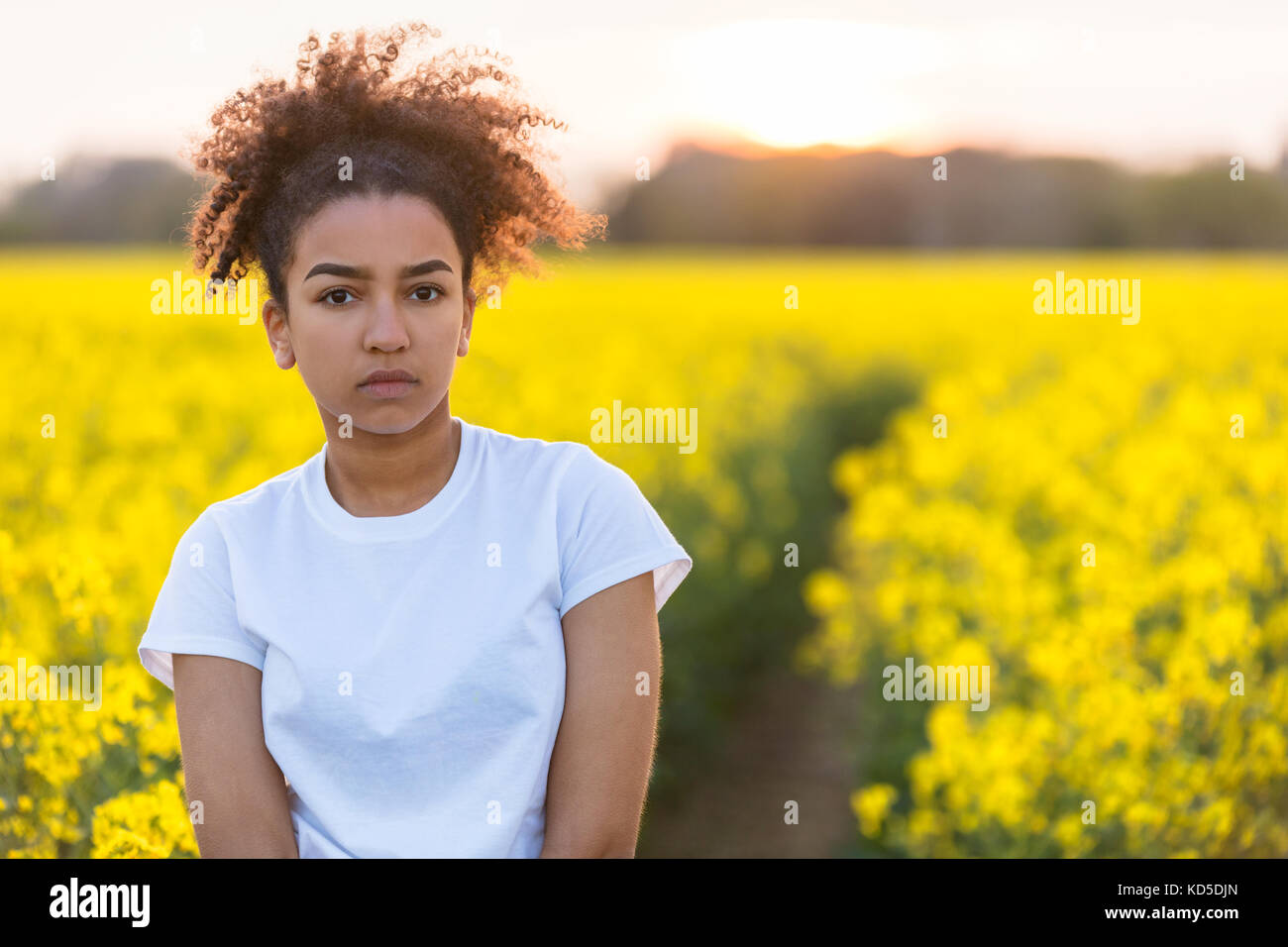 Schönen gemischten Rennen african american girl Teenager weibliche junge Frau traurig, deprimiert oder am Ende eines Pfad nachdenklich in einem Feld von gelben Blumen Stockfoto