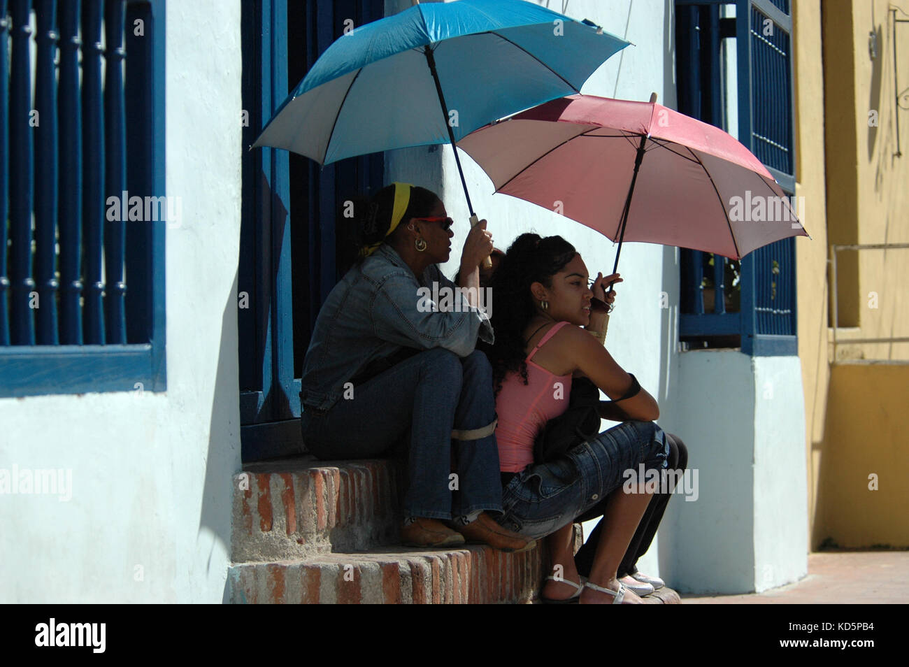 Kubanische junge Frauen sitzen auf der Treppe mit Sonnenschirmen für Schatten, Camagüey, Kuba Stockfoto