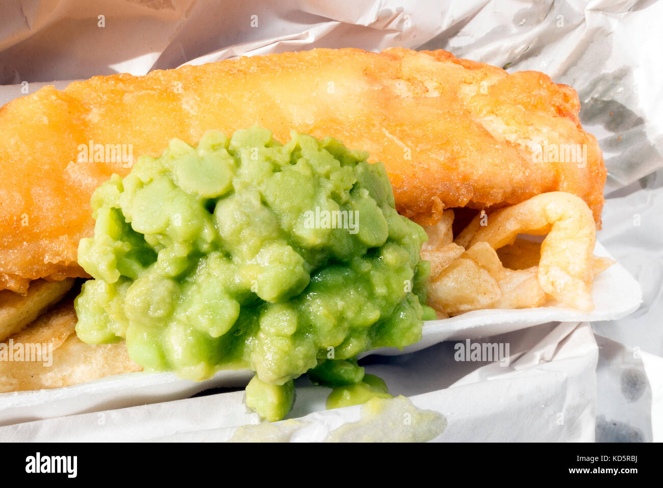 Fisch und Chips mit Erbsenpüree, Papier aus einem Takeaway, UK gewickelt. Stockfoto
