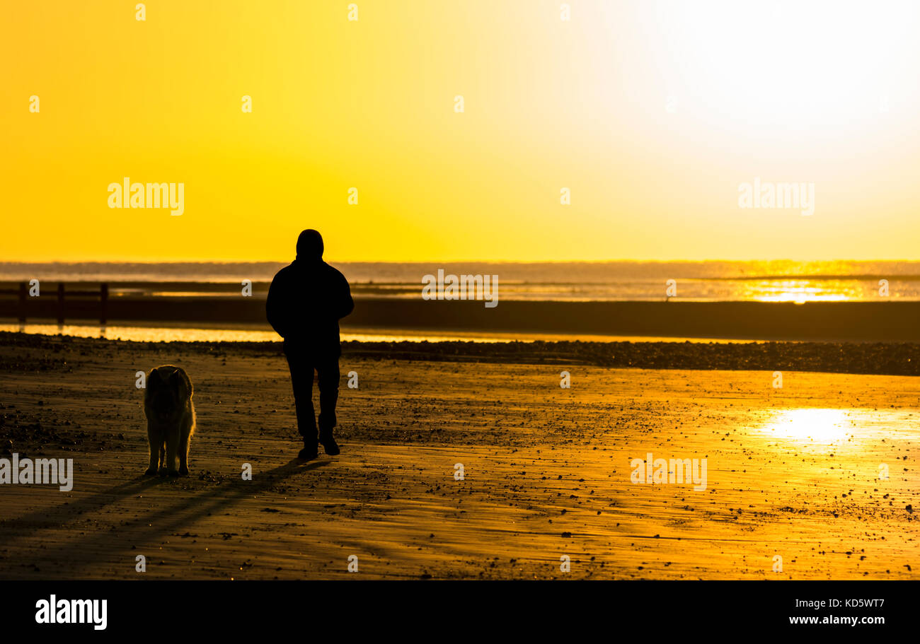 Silhouette eines Mensch und Hund am Strand, wenn die Sonne aufgeht in Großbritannien. Stockfoto