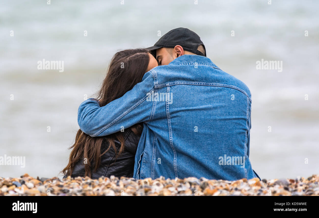Junges Paar sitzt auf einem Strand küssen und umarmen einander. Junge Geliebte umarmen am Strand. Stockfoto