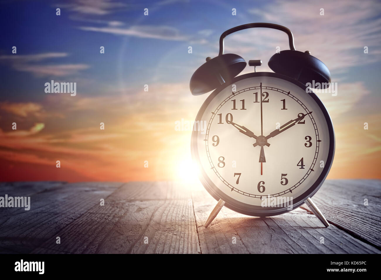Wecker auf Holztisch bei Sonnenuntergang Stockfoto