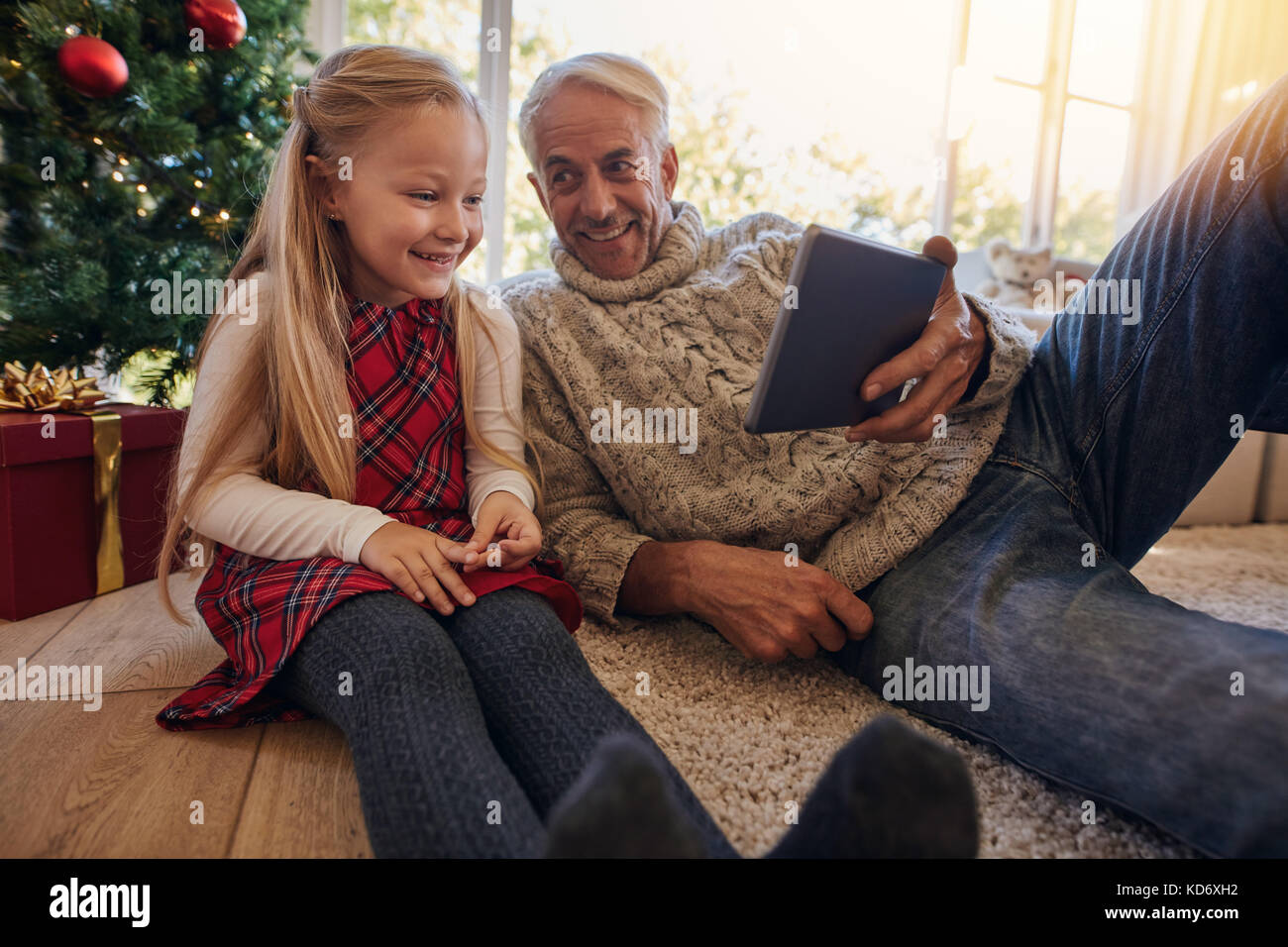 Großvater und Enkelin sitzen auf dem Boden und auf digitalen Tablet während der Weihnachtszeit. Mann mit seinem kleinen Mädchen in ein Video auf digitale Tabl Stockfoto