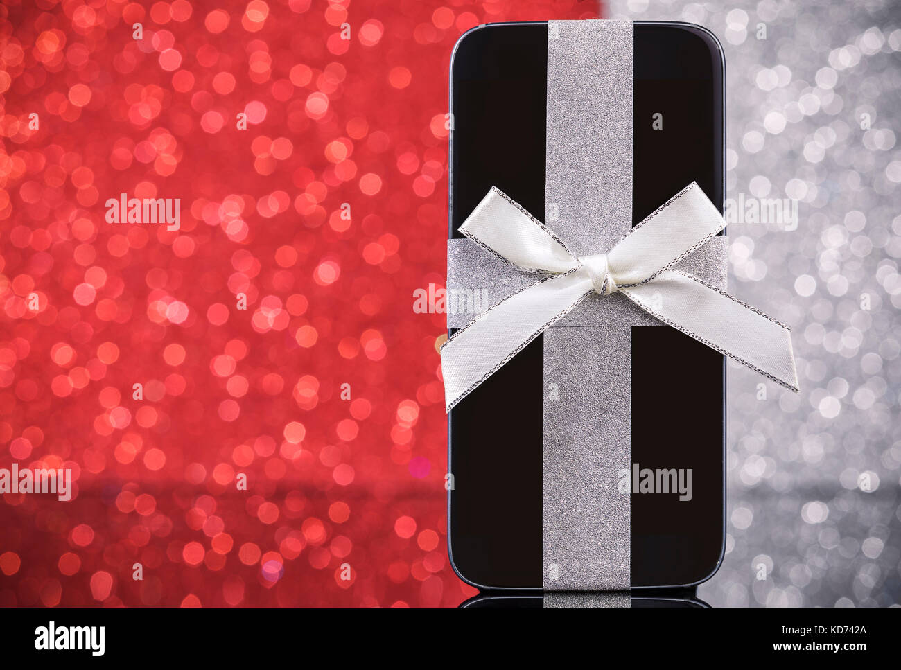 Smartphone für Weihnachtsgeschenk auf schwarzem Glas Tisch über Rot und Silber Hintergrund. Fokus auf dem Smartphone. Stockfoto