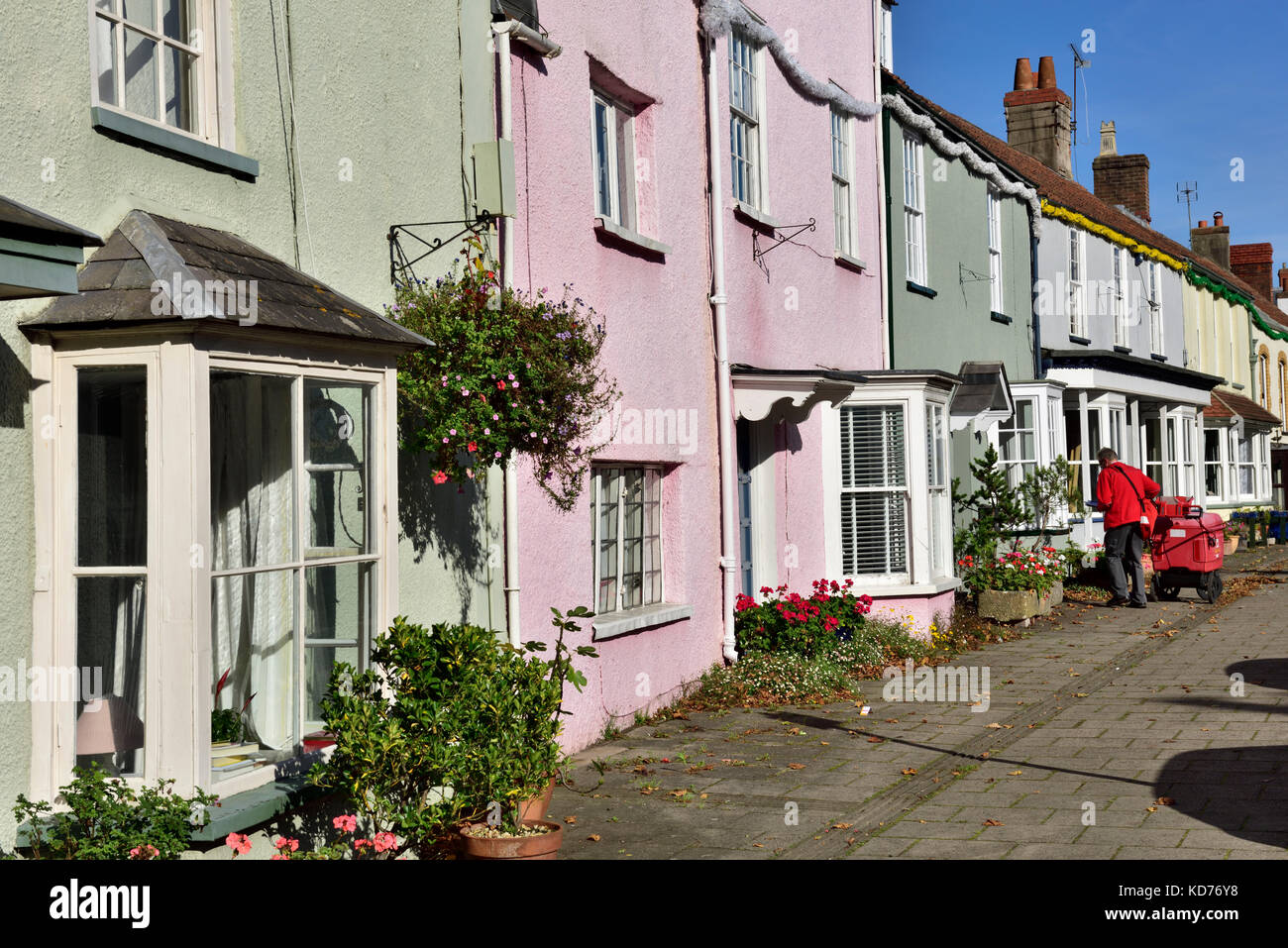 Postman die Lieferungen auf Umläufen in der Zeile von terrassenhäusern an der High Street in der kleinen englischen Stadt Thornbury, South Gloucestershire Stockfoto