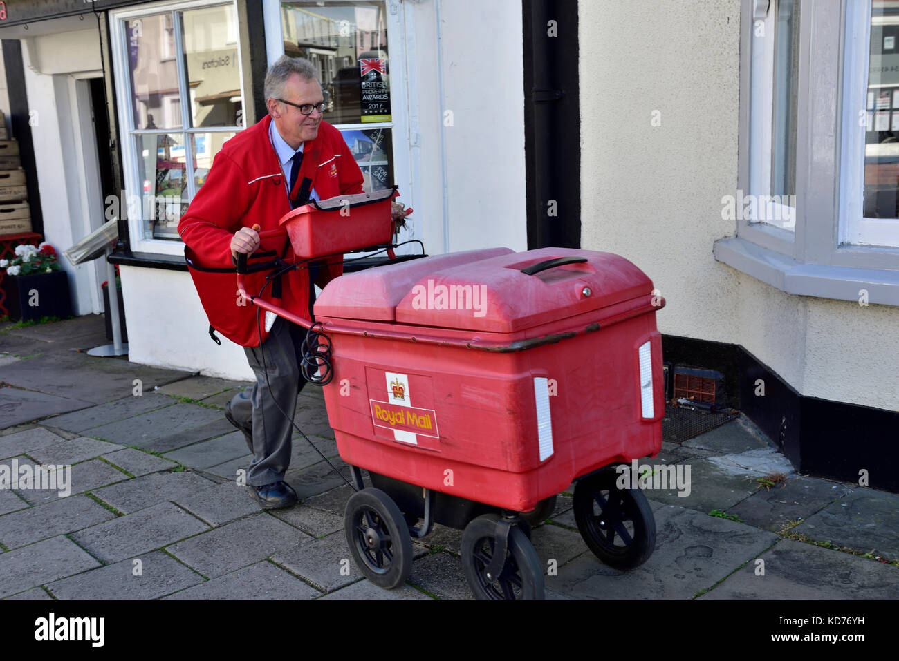 Postman drücken Warenkorb die Lieferungen auf Umläufen in der kleinen englischen Stadt Thornbury, South Gloucestershire Stockfoto