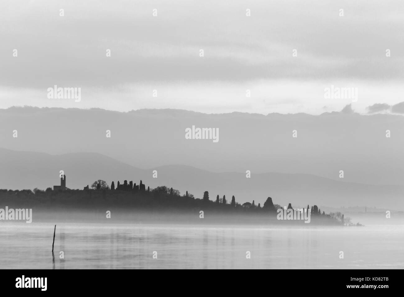 Ein See in der Abenddämmerung, mit schönen, weichen Töne in den Himmel und Wasser und eine Insel mit Gebäuden in der Mitte des Nebels Stockfoto