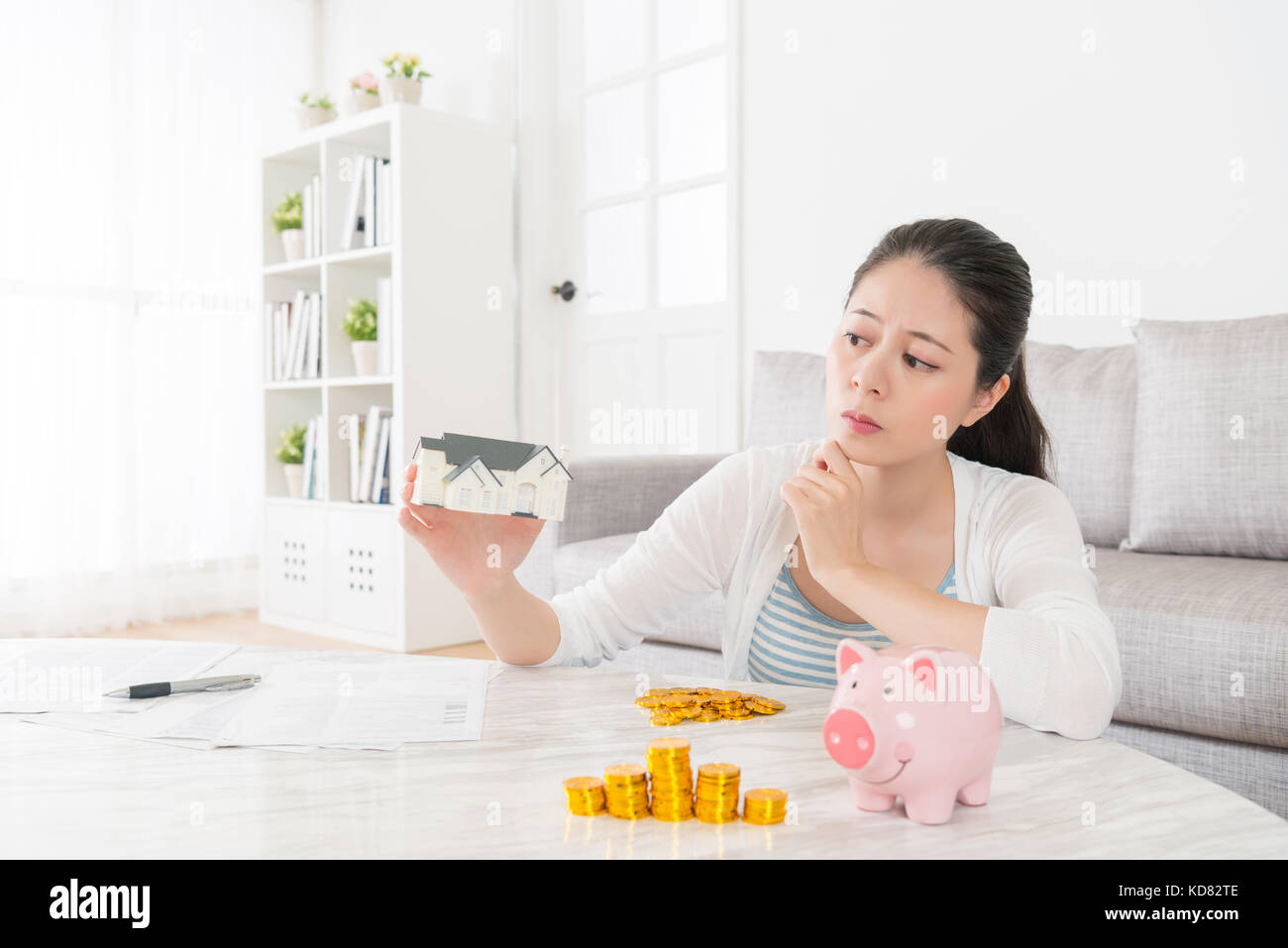 Schöne hübsche Mädchen Frau little house Modell suchen am Denken wie man das Sparen von Geld für den Kauf neuer Wohnung sitzen auf Wohnzimmer mit pigg Stockfoto