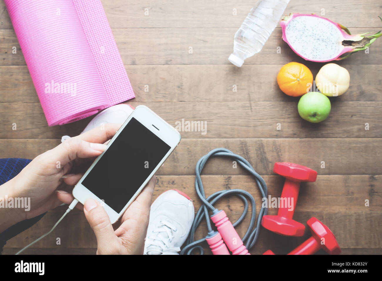 Frau in Sportbekleidung mit Handy mit Obst und Sport Anlagen im Hintergrund, Ansicht von oben Stockfoto