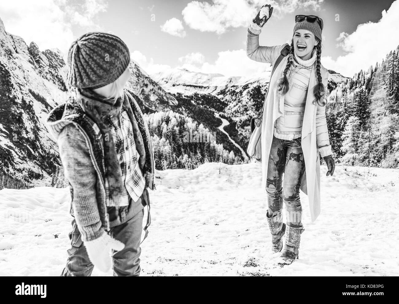 Winter auf höherer Ebene Spaß. Moderne Mutter und Kind Reisenden vor Bergkulisse in Alto Adige, Italien spielt Schneebälle Stockfoto