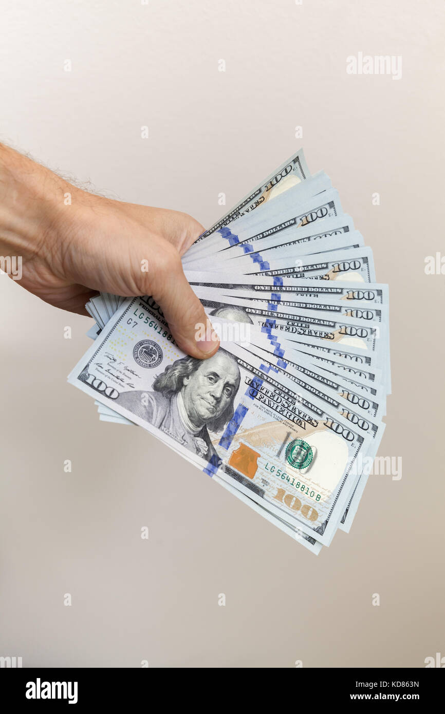 Fan von 100 Dollar Noten in männlicher Hand über graue Wand Hintergrund, vertikale Foto Stockfoto