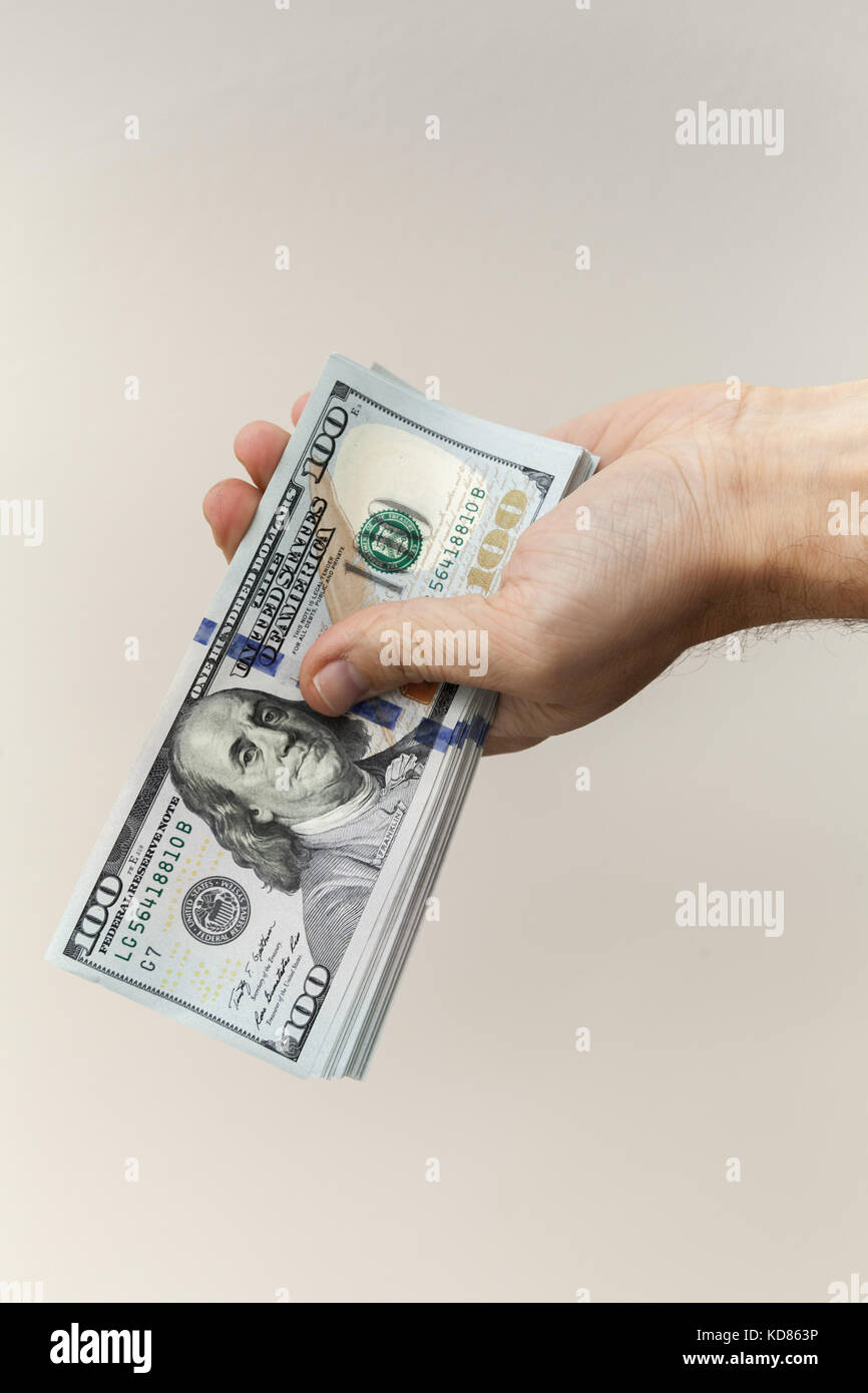 Bündel von einhundert Dollar Noten in männlicher Hand über graue Wand Stockfoto