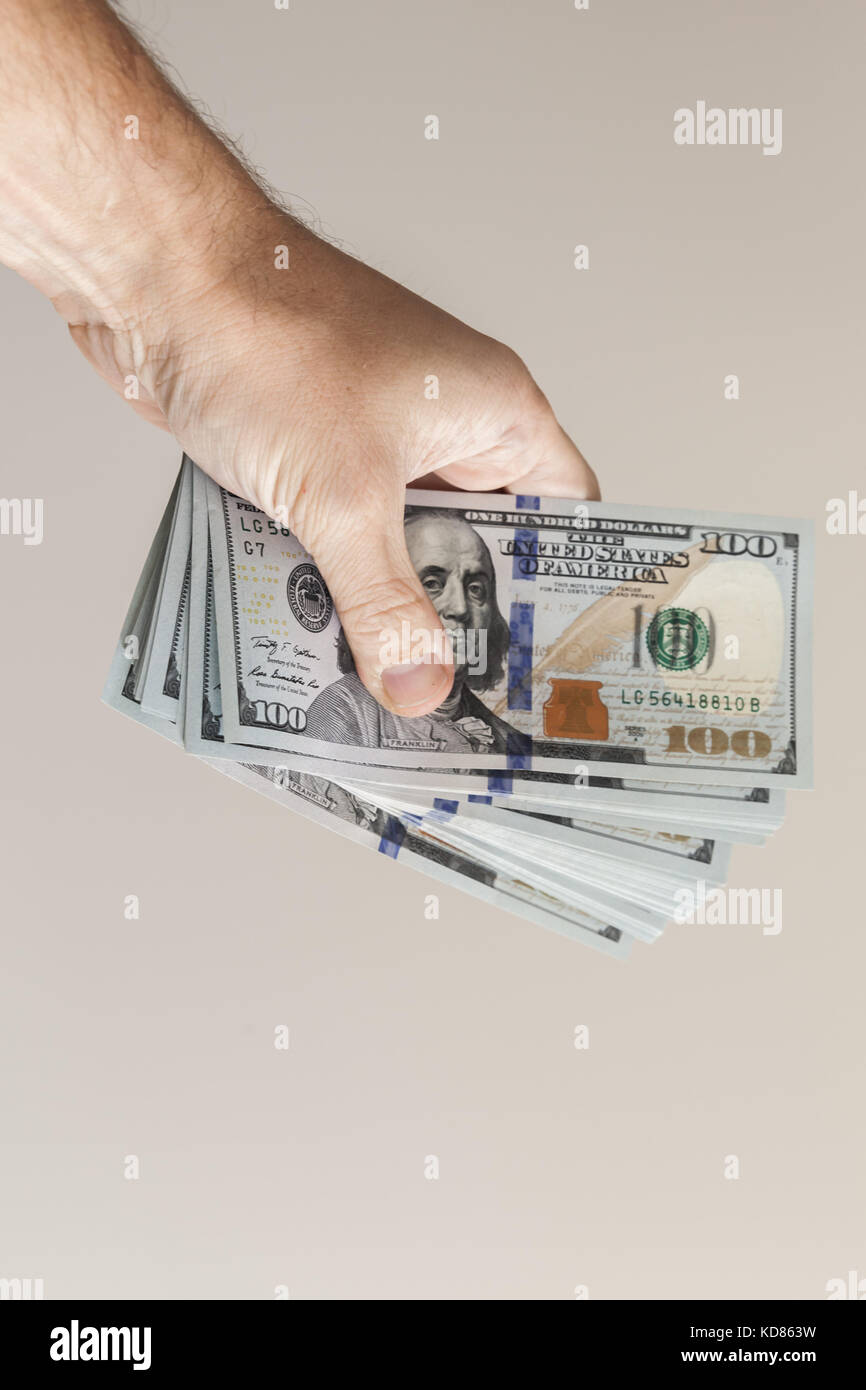 Vertikale Foto. Ventilator von einhundert Dollar Noten in männlicher Hand über graue Wand Hintergrund Stockfoto