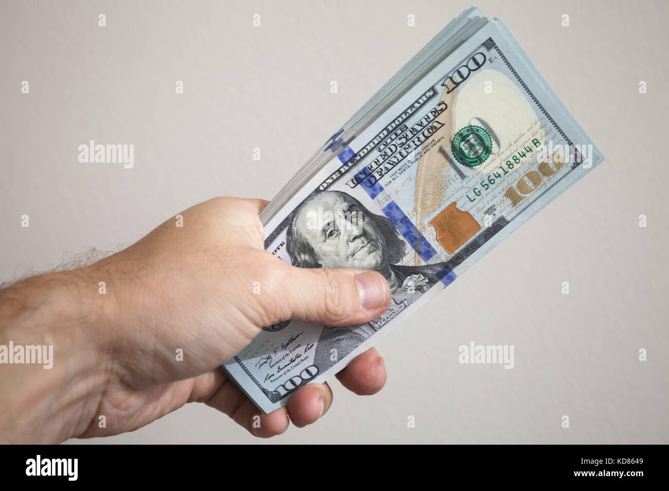 Bündel von einhundert Dollar Noten in männlicher Hand über graue Wand Hintergrund Stockfoto