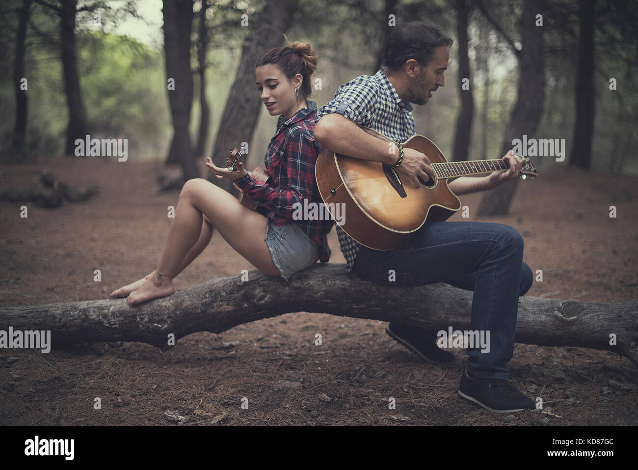 Mann und Mädchen sitzen im Wald und spielen Gitarre und Ukulele, Spanien Stockfoto