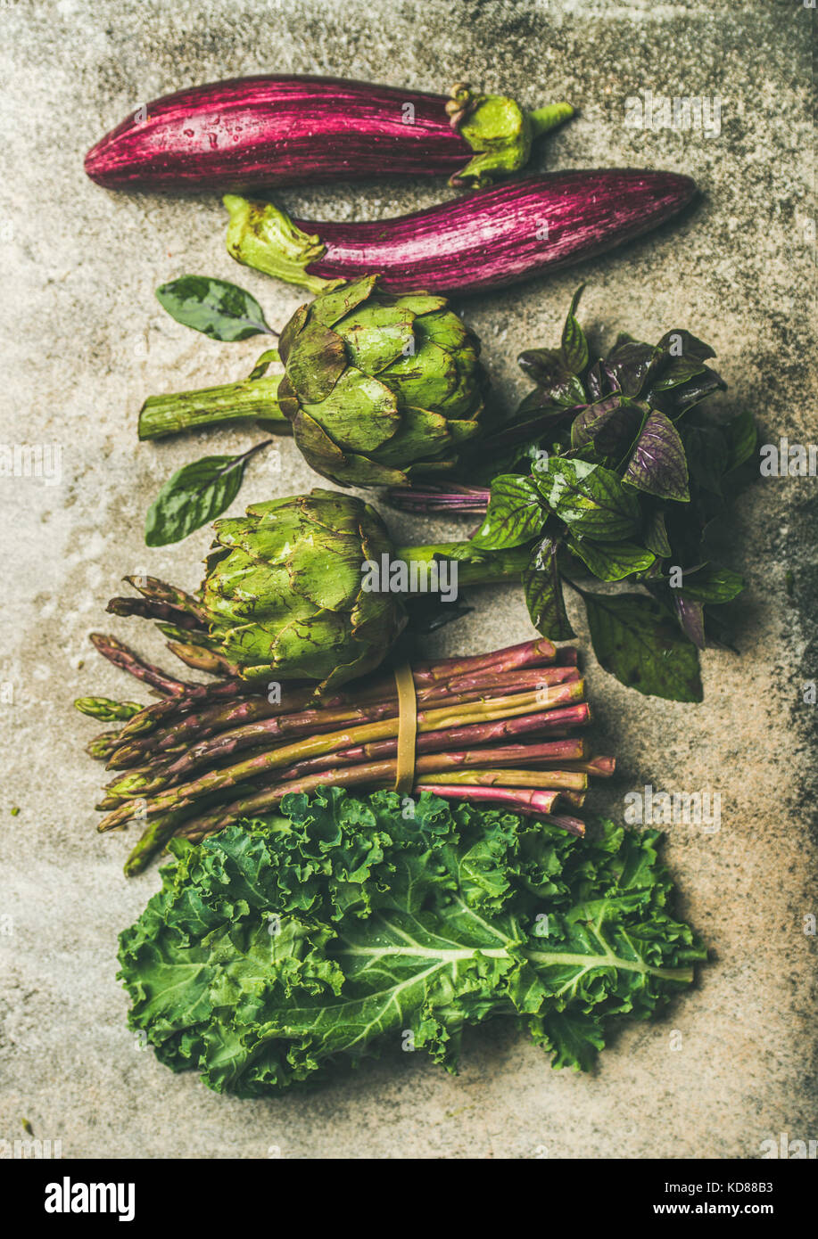 Flachbild-lay von Grün und Violett frisches Gemüse Vielfalt über konkreten Hintergrund, Ansicht von oben. Lokalen, saisonalen Produkten für gesundes Kochen. Eggplans, Bohnen, Stockfoto