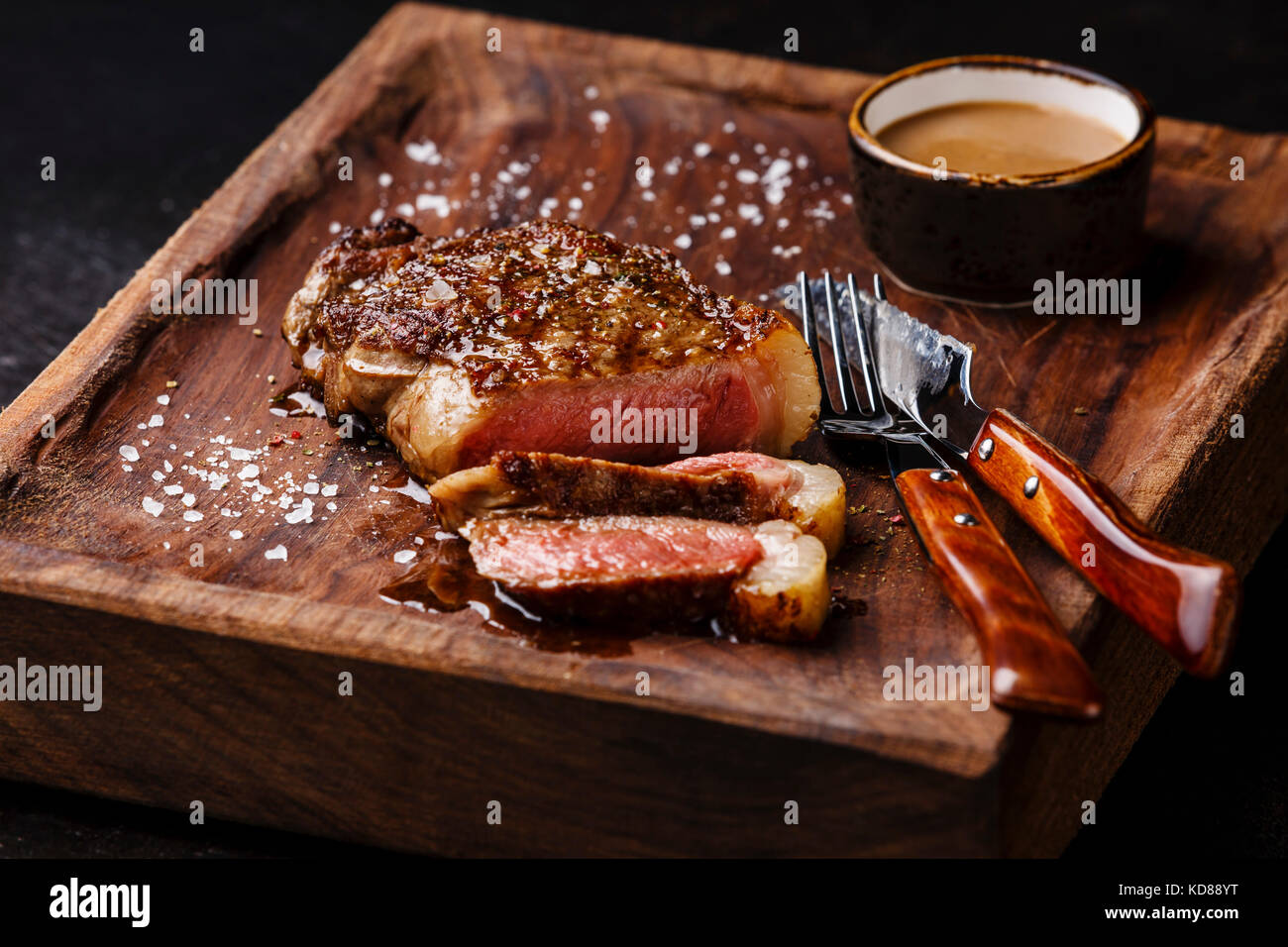 Geschnetzeltes Fleisch vom Grill Steak New York Roastbeef mit Pfeffersauce  und Messer und Gabel auf Holzbrett auf schwarzem Hintergrund  Stockfotografie - Alamy