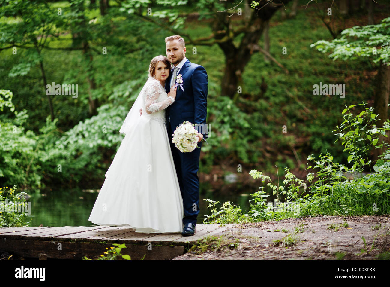 Attraktive Hochzeit paar stehen und auf eine kleine Holzbrücke posiert