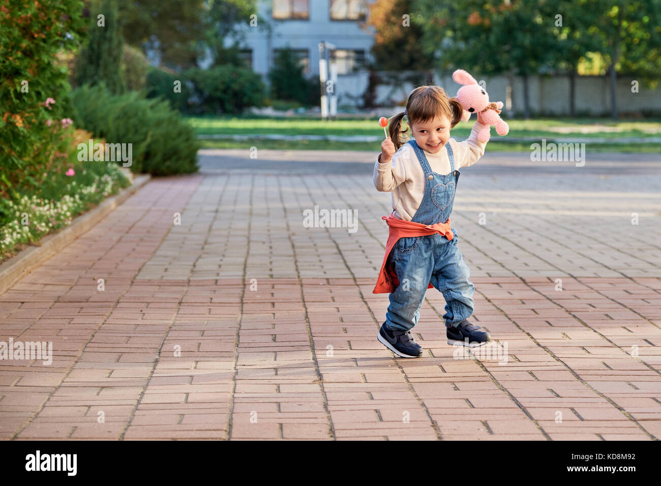 Lustige kleine Mädchen vor Freude hüpfend. Ein junges Kind in Jeans Overalls Stockfoto