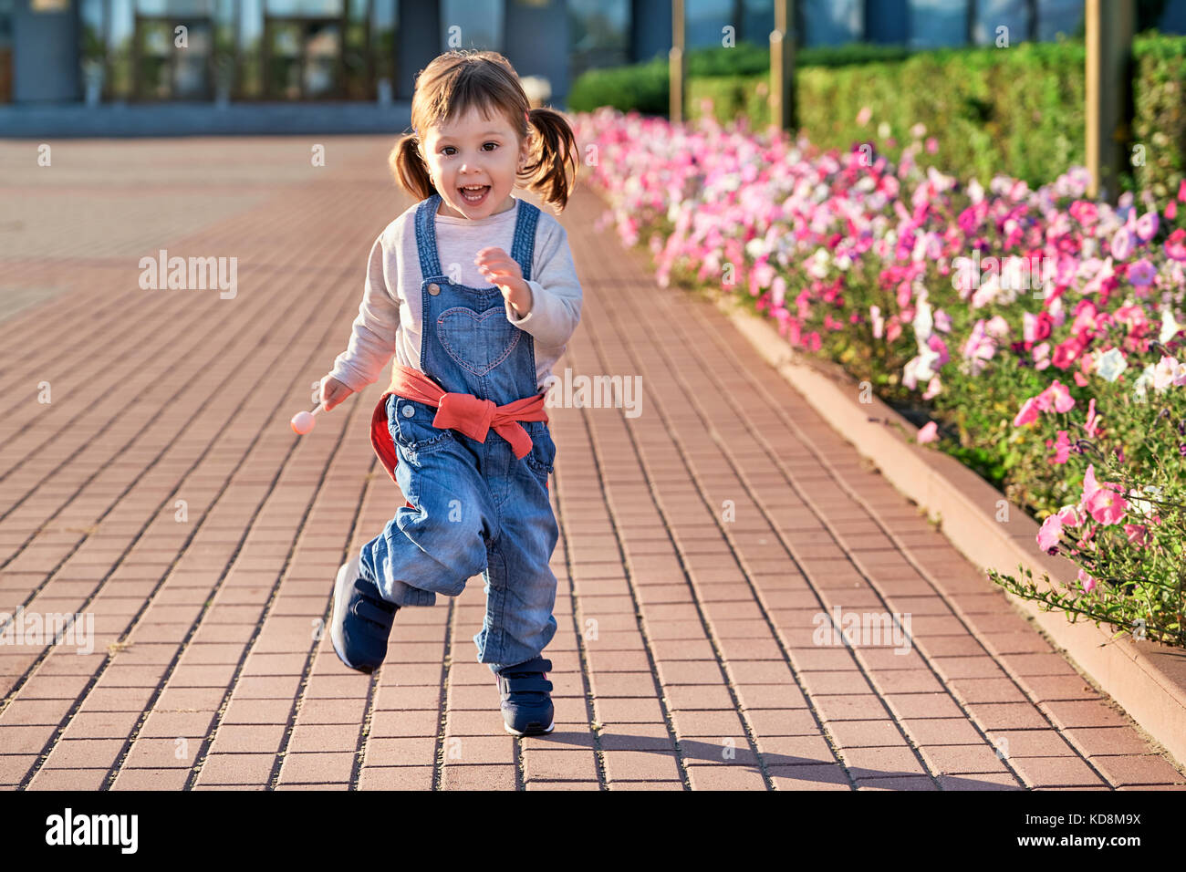 Lustige kleine Mädchen vor Freude hüpfend. Kleines Mädchen in Jeans Overall. Stockfoto