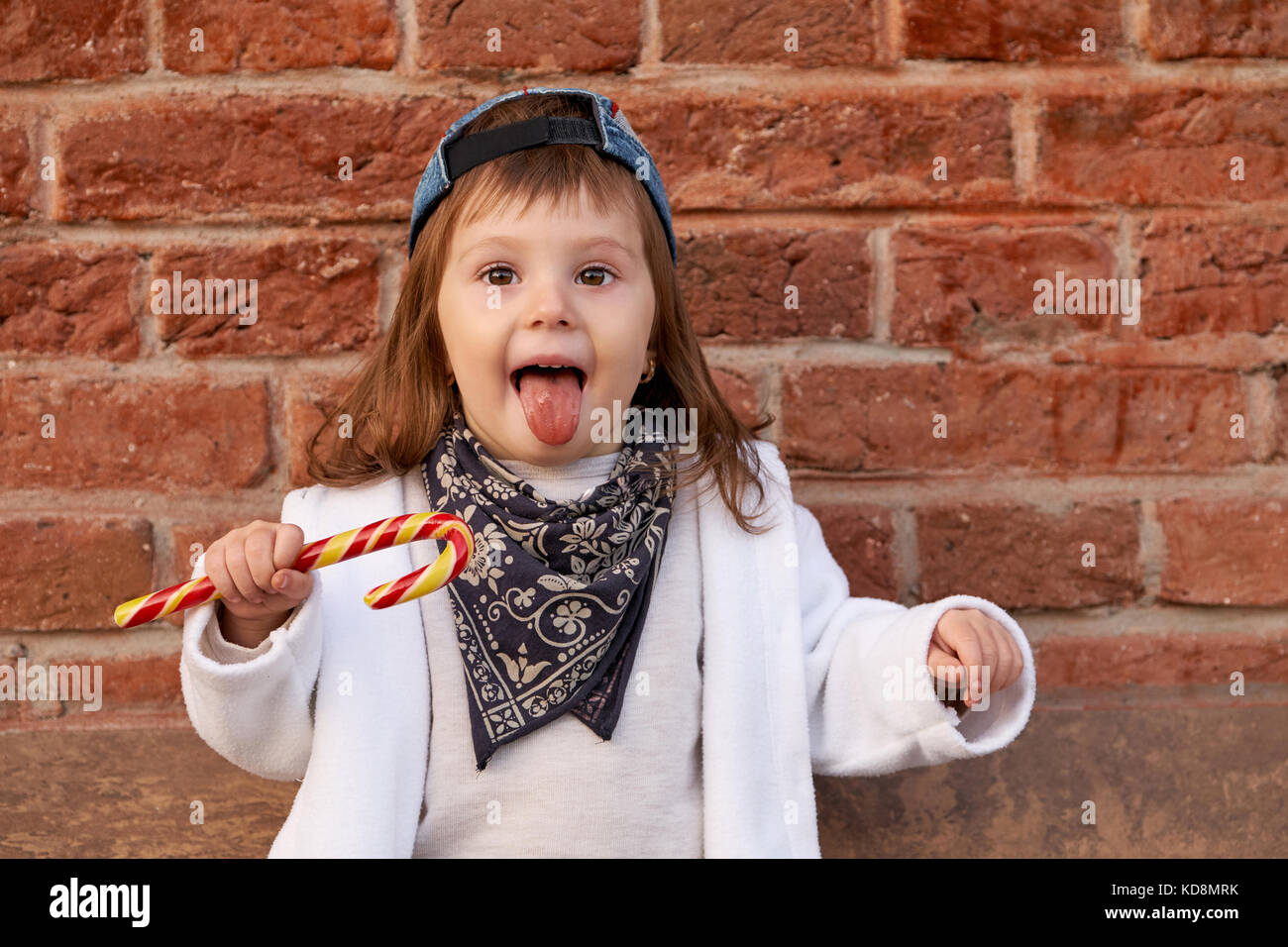 Nett schön Kind isst Süßigkeiten. Kleines Mädchen zeigt Zunge Stockfoto