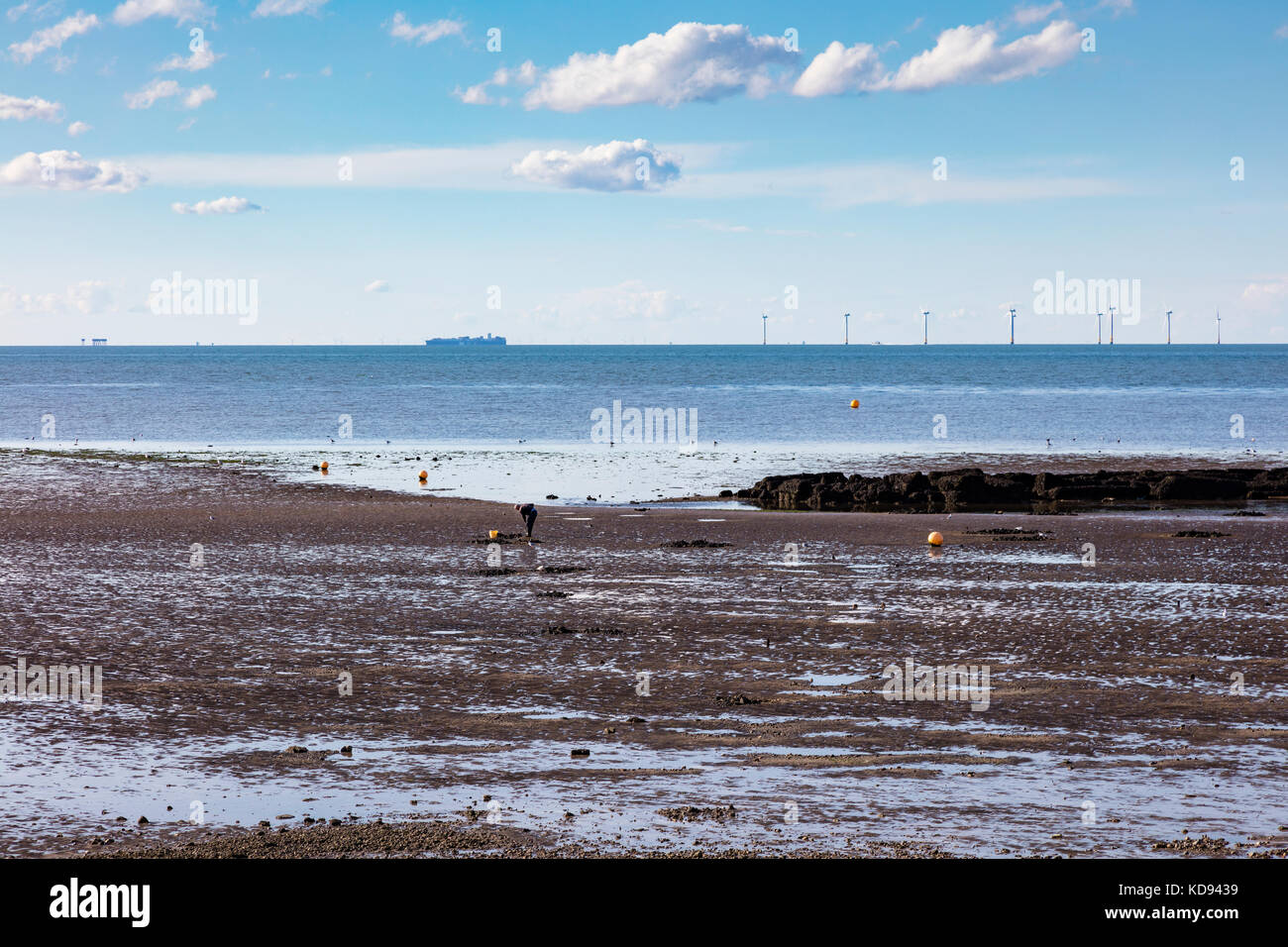 Ein Köder-Digger am Ufer bei Ebbe in der Abenddämmerung in Hampton, Herne Bay, Kent. Ein Schiff und Windturbinen befinden sich am trüben Horizont. Stockfoto