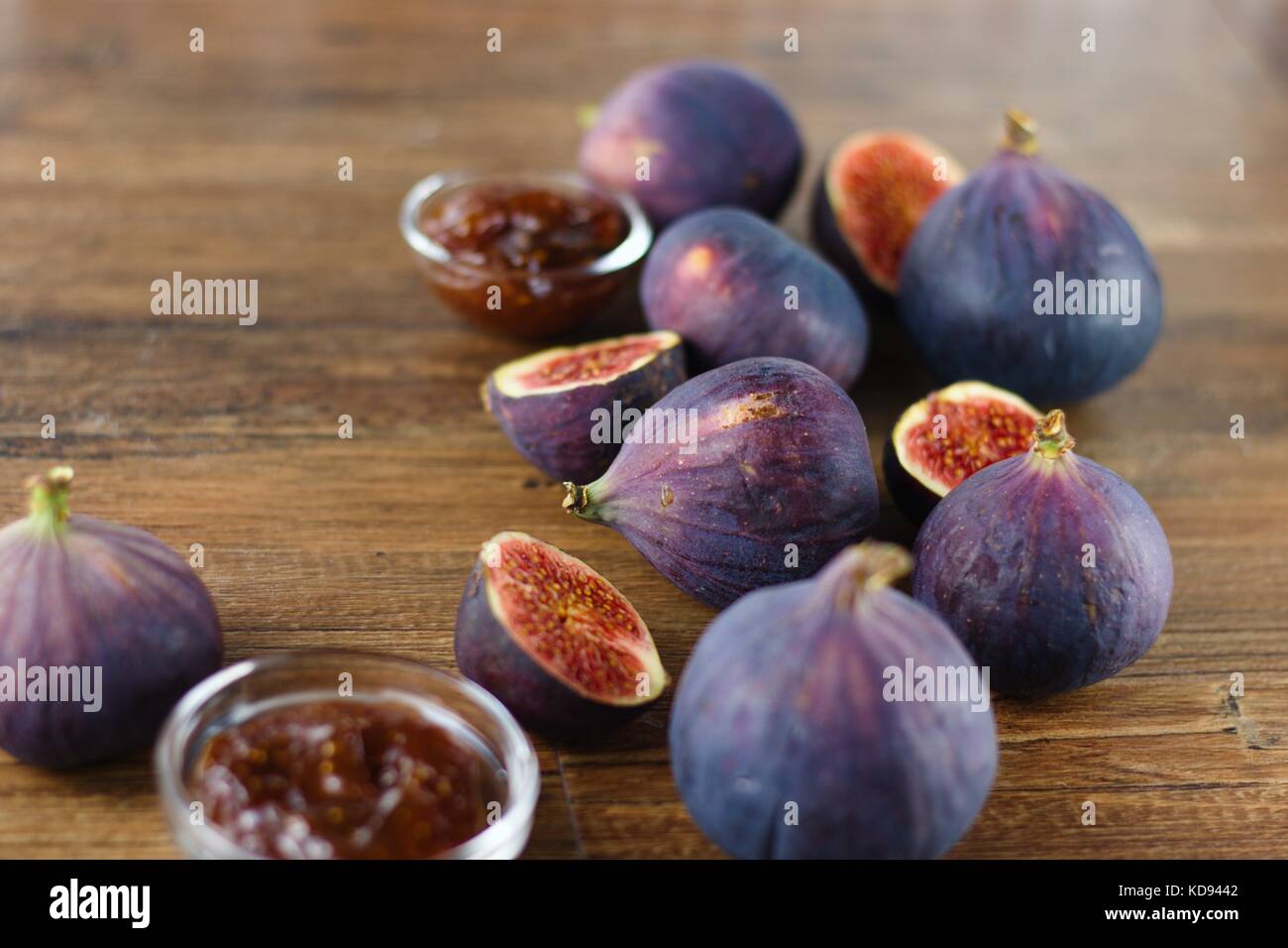 Reif, blau und lila Feigen, ganz und halbiert, zufällig auf dunklem Holz Tisch unter Glas verschüttet Schüsseln Feigenmarmelade Stockfoto