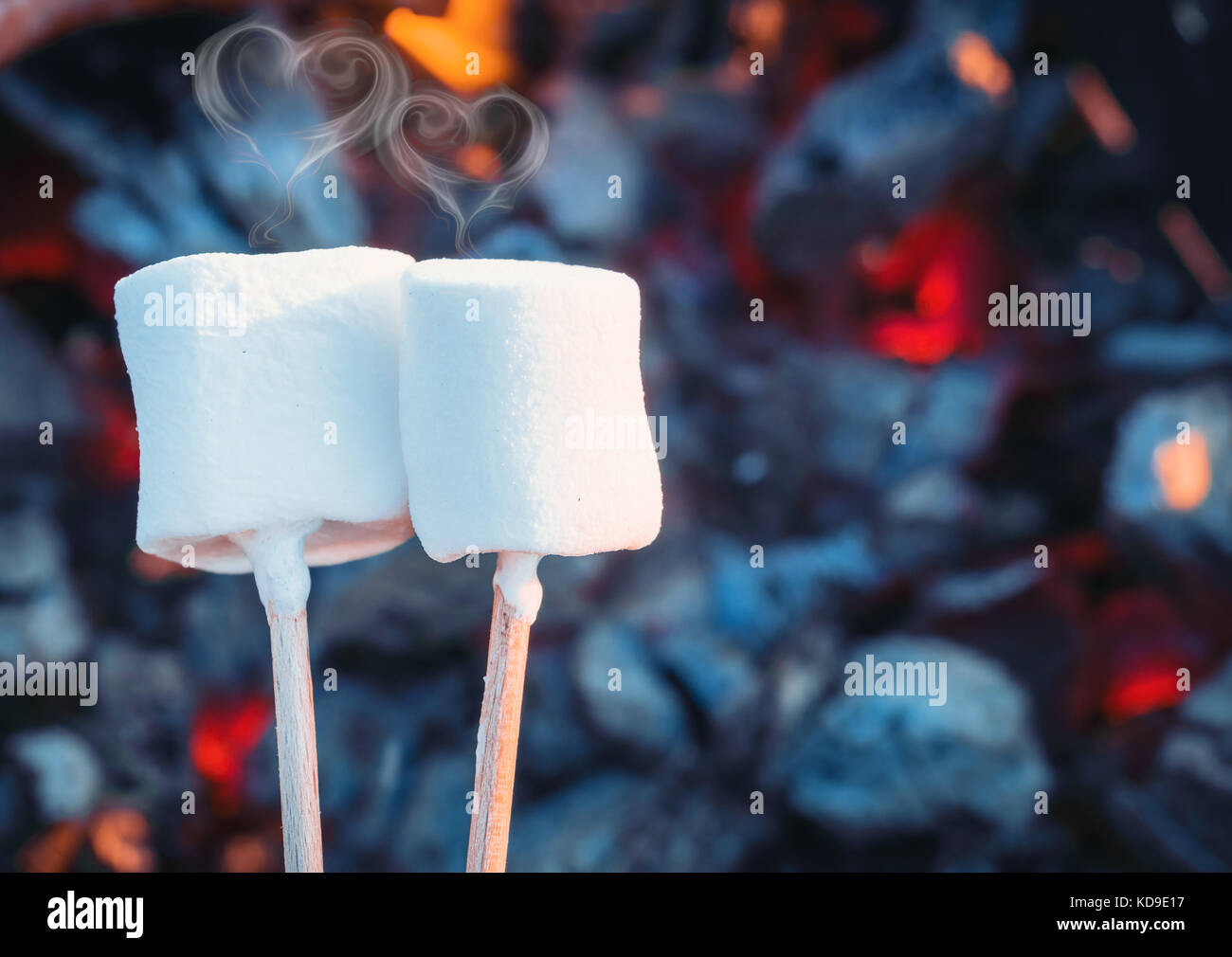 Zwei weiße süßen Marshmallows rösten über Feuer flammen. Rauch in Form von Herzen. eibisch am Spieß gebraten auf Holzkohlen Stockfoto