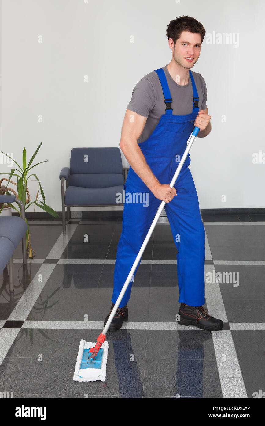 Portrait des jungen Mannes, den Boden mit Mop im Büro Stockfoto