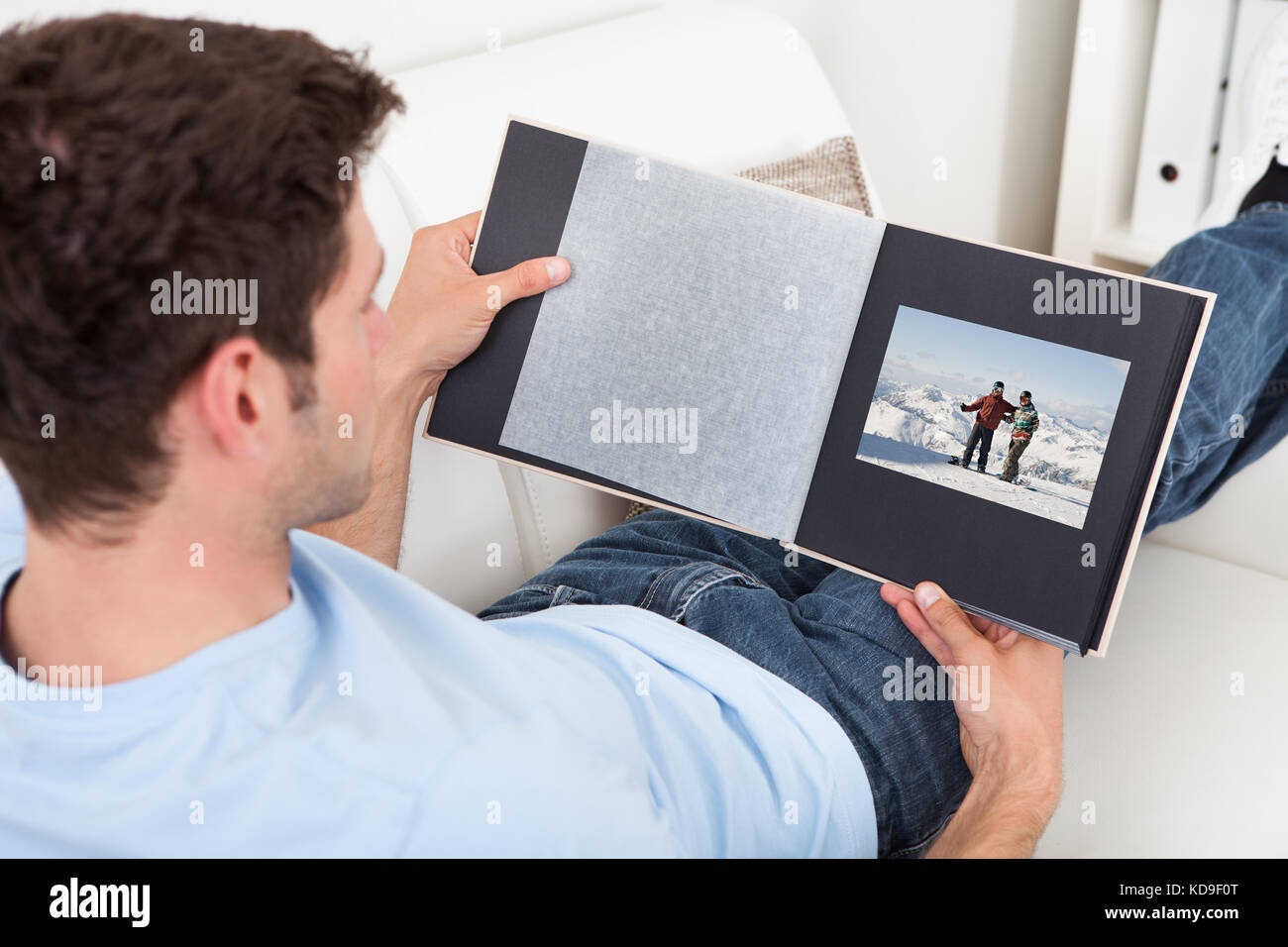 Junger Mann sitzt auf der Couch Fotoalbum betrachten Stockfoto
