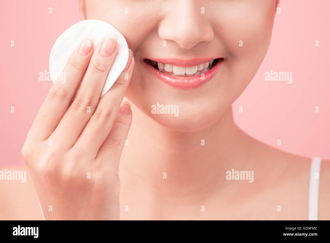 Wunderschöne junge Frau mit Wattebausch und lächelnd in die Pflege von ihr Gesicht für frische, gesunde Hautpflege auf rosa Hintergrund Stockfoto